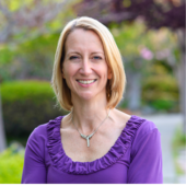 Photograph of a middle aged woman in a purple blouse with a blonde shoulder length bob.